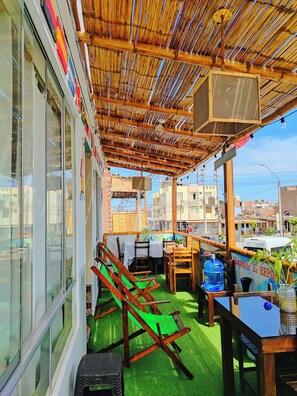 Un espace extérieur abrité, doté d’un toit en bambou, d’une table avec des chaises et offrant une vue sur le paysage urbain en arrière-plan.