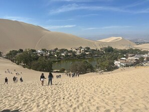 Eine Wüstenlandschaft mit Sanddünen, einem kleinen See und einer Stadt mit Gebäuden.