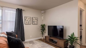 Een woonkamer met een bank, televisie en potplanten.