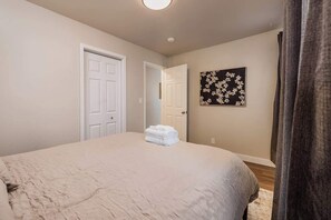 Un dormitorio con una cama, dos puertas, un cuadro colgado en la pared y una ventana con cortinas.