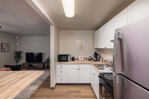 Una cocina moderna con armarios blancos, un refrigerador de acero inoxidable, un microondas y una estufa.