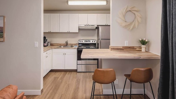 Een moderne keuken met witte kasten, een houten aanrecht, een kookplaat en twee bruine stoelen.