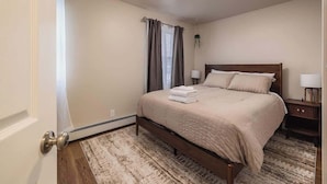 Een netjes opgemaakt slaapkamer met een bed, nachtkastjes en een raam met gordijnen.