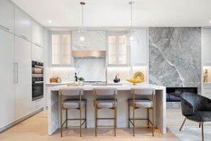 A modern kitchen with marble countertops, bar stools, pendant lights, and a fireplace. - Luxury 4BR | High Park, Beach & Lake Views | Toronto (Toronto)