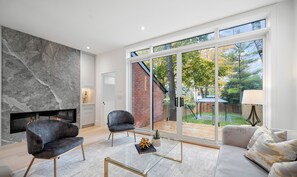 A modern living room with a fireplace, two grey armchairs, a glass coffee table, and a sofa with patterned cushions. - Luxury 4BR | High Park, Beach & Lake Views | Toronto (Toronto)