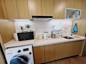 Une cuisine compacte équipée d’un four à micro-ondes, d’une machine à café et d’un lave-linge.