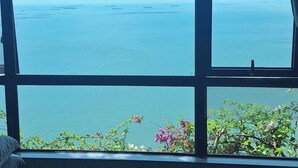 A view through a window with a clear sky and calm sea, with some greenery at the bottom.