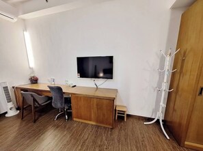 Une pièce comprenant un bureau en bois, un téléviseur fixé au mur, un porte-manteau et un petit tabouret.