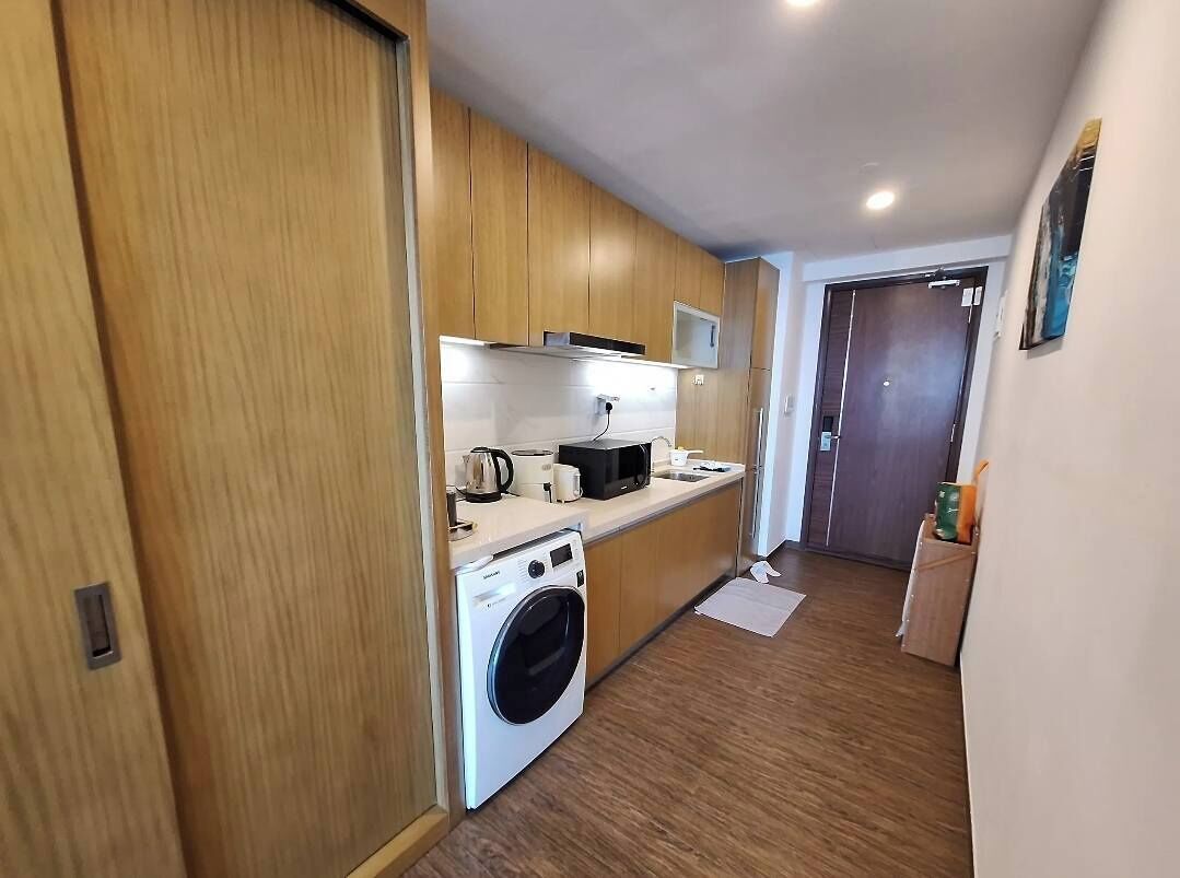 A compact kitchen with wooden cabinets, a washing machine, and a microwave.
