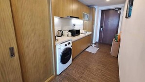 A compact kitchen with wooden cabinets, a washing machine, and a microwave.