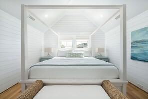 A bedroom with a canopy bed, two bedside tables, a window, and a painting on the wall. - Bald Head Island retreat, where coastal elegance meets relaxed island living (Bald Head Island)