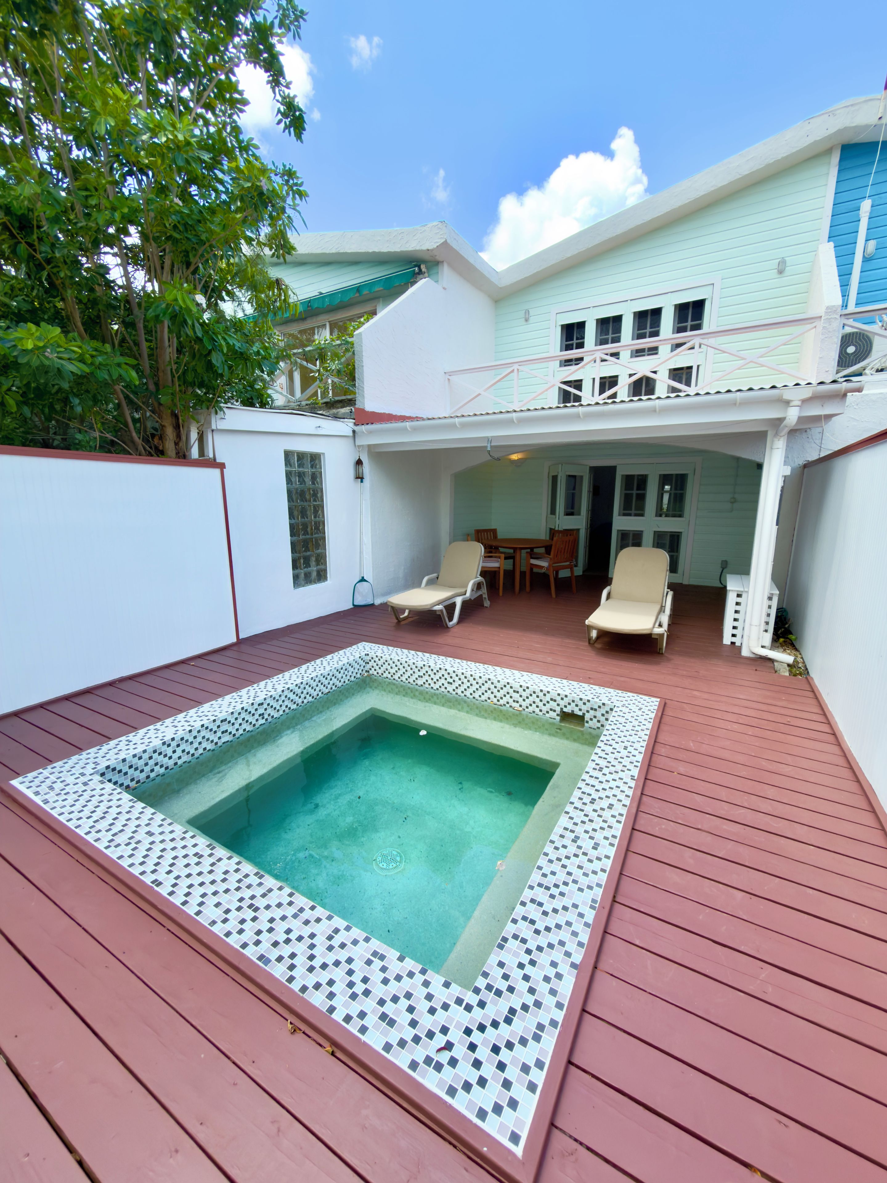 A pool area with a hot tub, wooden deck, and a covered seating area with chairs.