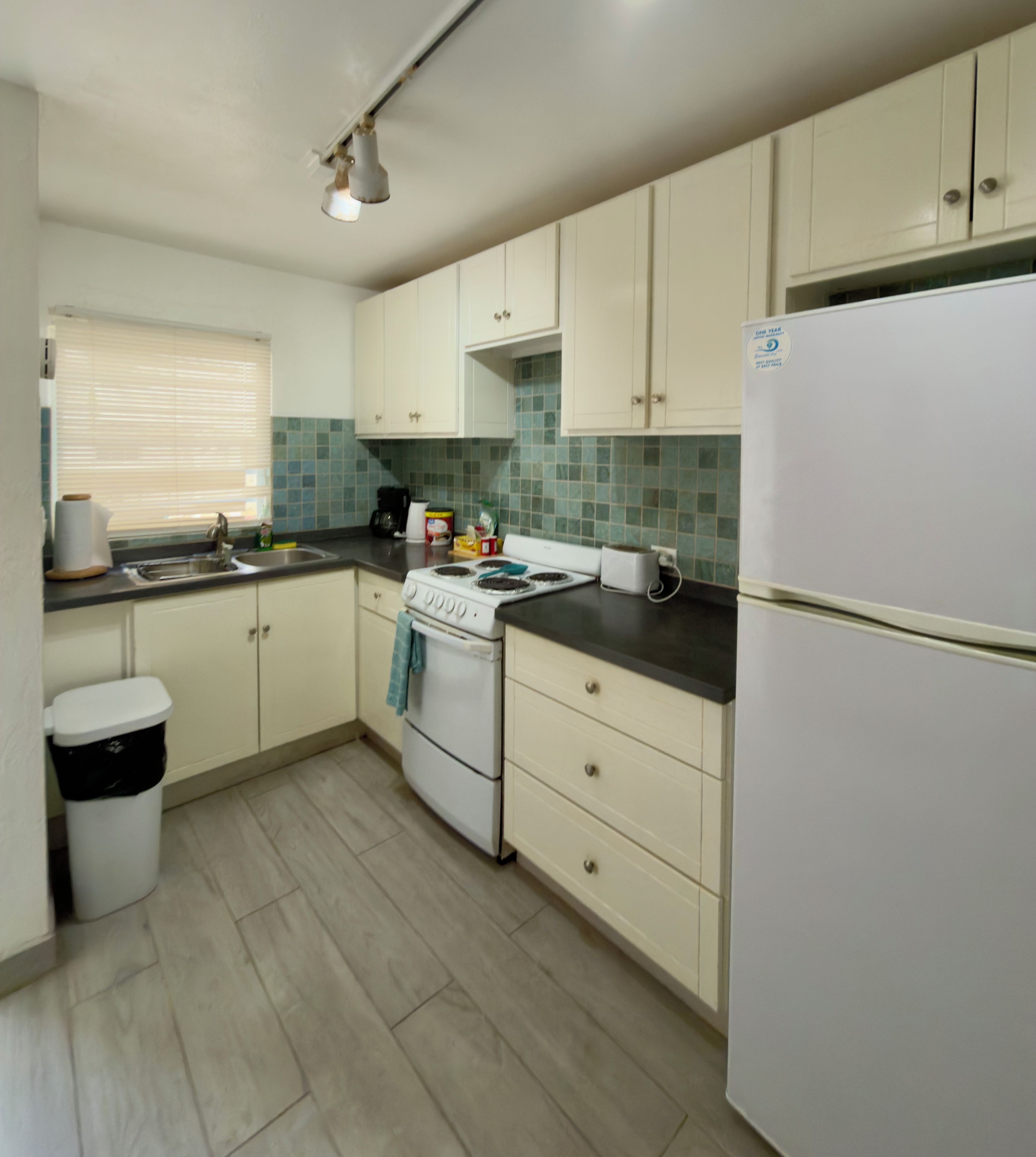A compact kitchen with white cabinets, a stove, a sink, and a refrigerator.