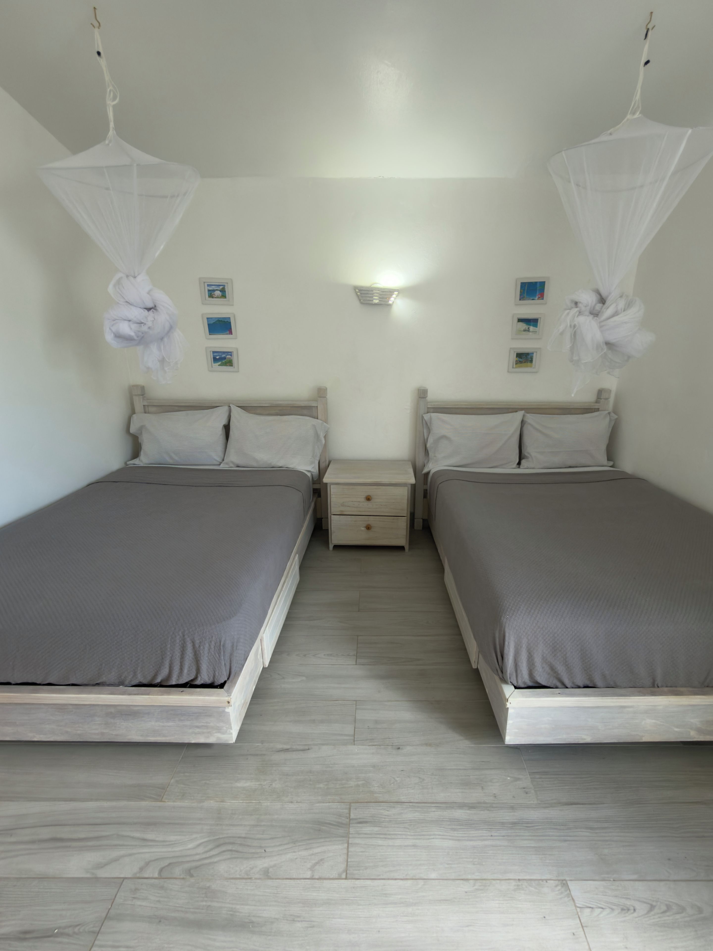 Ein Doppelzimmer mit zwei Betten, einem Nachttisch, einer Wandleuchte und einem Deckenventilator.