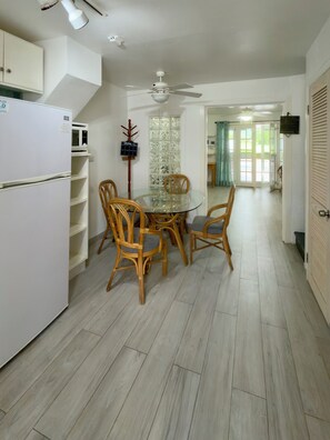 Een eethoek met een glazen tafel, omringd door stoelen, een witte koelkast en een magnetron.