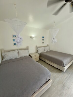 Een slaapkamer met twee bedden, een nachtkastje, een wandlamp en een klamboe.