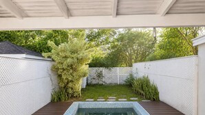 Ein rechteckiger Pool mit Fliesenrand, umgeben von einer Holzterrasse und weißen, strukturierten Wänden.