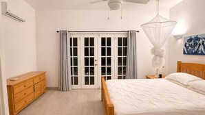 Ein Schlafzimmer mit einem hölzernen Bett, einem Nachttisch, einer Kommode, einem Deckenventilator und einem Fenster mit Vorhängen.