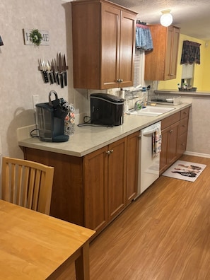 A kitchen with wooden cabinets, a coffee maker, a sink, and a dining area with a chair and table. - Spend a night on a farm. (Scottsdale)