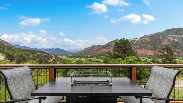Een balkon met een tafel en stoelen met uitzicht op een bergachtig landschap.