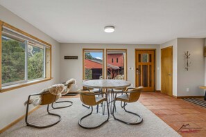 Ein Zimmer mit einem runden Tisch, vier Stühlen, einem Fenster mit Blick auf Bäume und einer zur Außenseite führenden Tür.