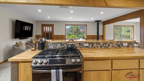 Een moderne keuken met een groot eiland, houten balken, een steen rugpaneel en uitzicht op groen.