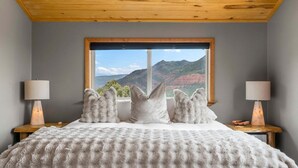 Een slaapkamer met een groot bed, een raam met uitzicht op de bergen, twee bedlampen en een houten plafond.