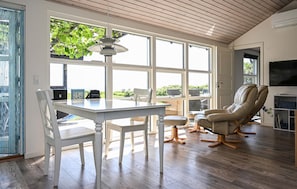 A spacious room with a large window, a dining table with chairs, a leather recliner, and a television.