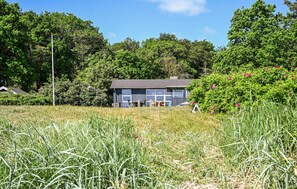 A small, single-story building with a dark roof, surrounded by lush greenery and trees.