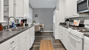 A modern kitchen with white cabinets, a granite countertop, a built-in oven, and a dining area with a chair and table. - Serene 4-bedroom house with AC in charming Alhambra (Alhambra)
