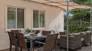 An outdoor patio with a table set for dining, wicker furniture, and a pergola with string lights. - Serene 4-bedroom house with AC in charming Alhambra (Alhambra)