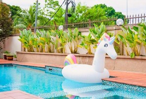 Une piscine avec un flotteur en forme de licorne blanche gonflable et un ballon aux couleurs de lâarc-en-ciel.