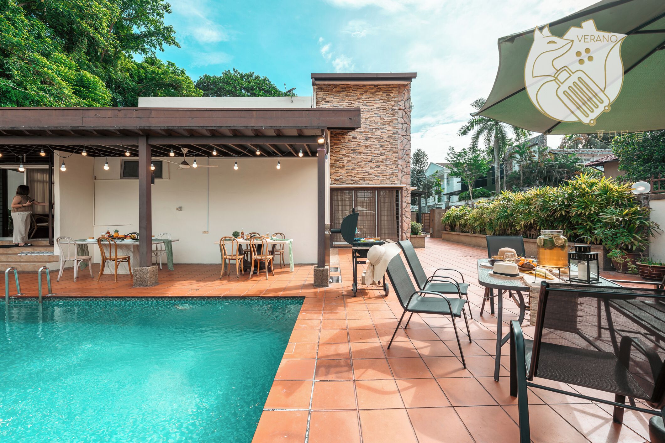 A poolside area with a covered seating area, outdoor tables, and a stone wall.