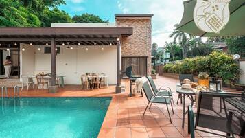 A poolside area with a covered seating area, outdoor tables, and a stone wall.