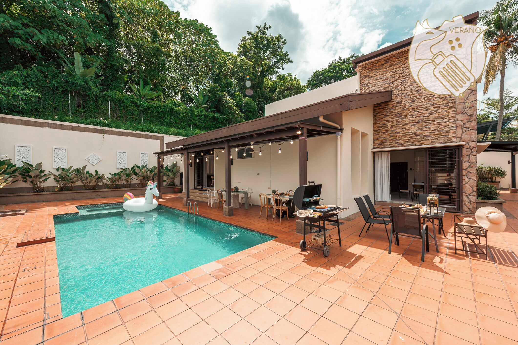 A swimming pool with a unicorn float, outdoor seating, and a covered patio area.