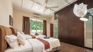 Habitación de hotel con dos camas, un ventilador de techo, un ventanal grande con cortinas y un armario.