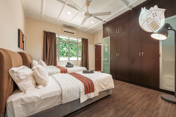 Quarto de hotel com duas camas, um ventilador de teto, uma janela grande com cortinas e um guarda-roupa.