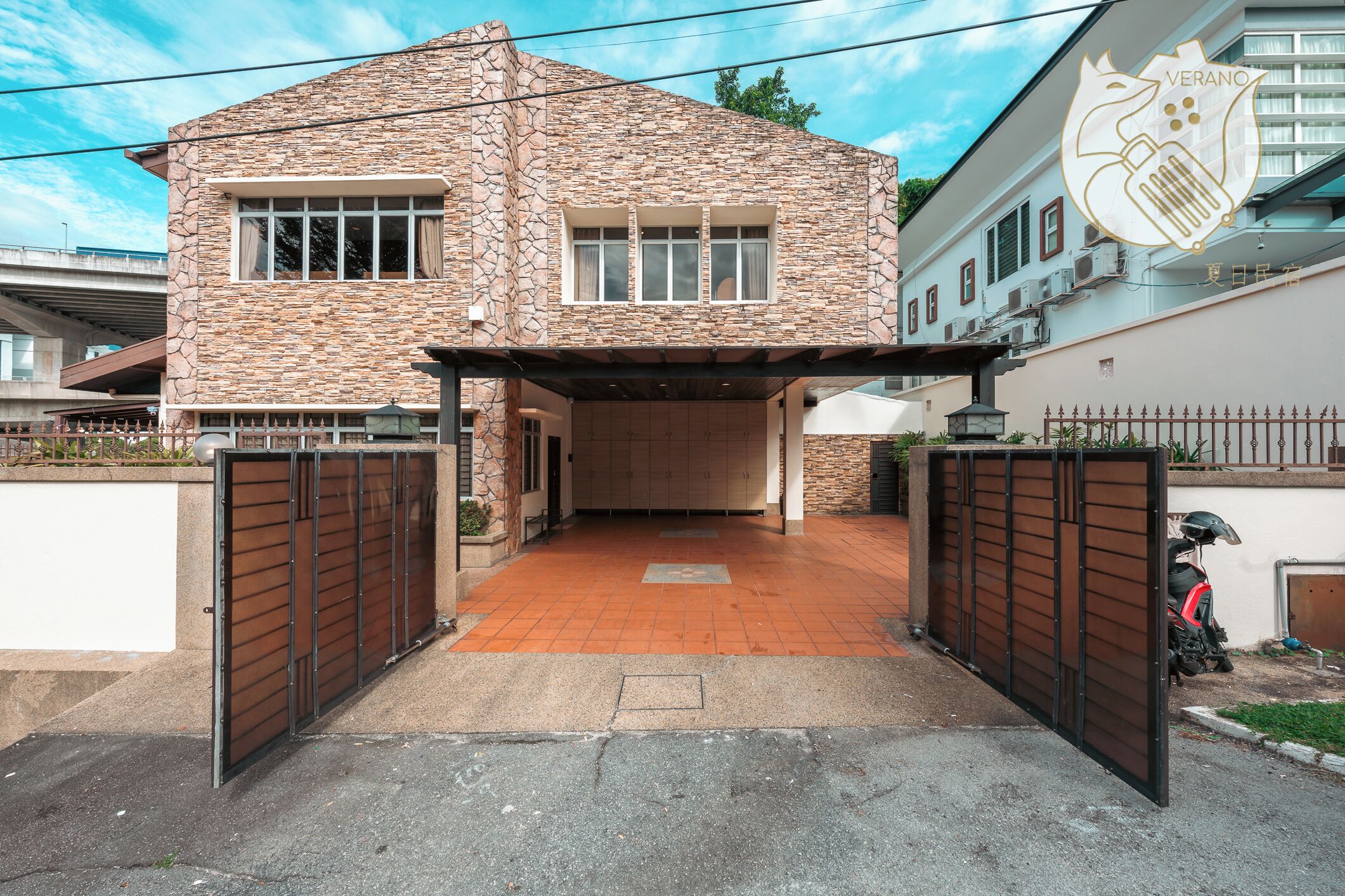 Une maison en pierre à deux étages, dotée d’une entrée fermée par un portail, d’une allée couverte et d’un scooter garé.