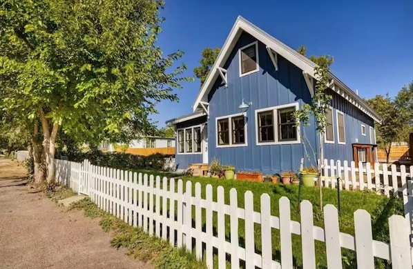 A blue house with a white picket fence, a driveway, and a tree.