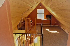 Habitación en ático con techo inclinado, escritorio, silla y lámpara colgante.