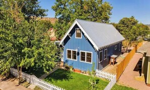 Una casa azul con valla de piquete blanca, un pequeño jardín y cielo despejado.