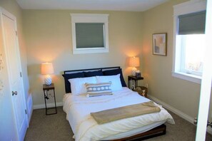 A bedroom with a bed, two bedside lamps, a window with blinds, and a framed picture on the wall. - The Blue House on Barr -Charming Cottage Retreat in the Heart of Canon City (Cañon City)