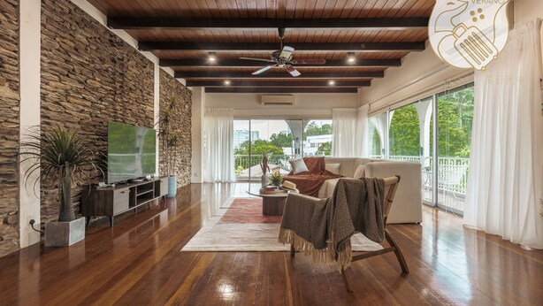 A spacious living room with a stone wall, wooden ceiling, and large windows.