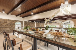 A dining area with a long table, chairs, and a stone wall.