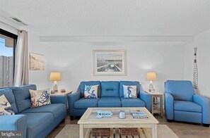 Ein Wohnzimmer mit zwei blauen Sofas, einem Couchtisch und einem gerahmten Bild an der Wand.