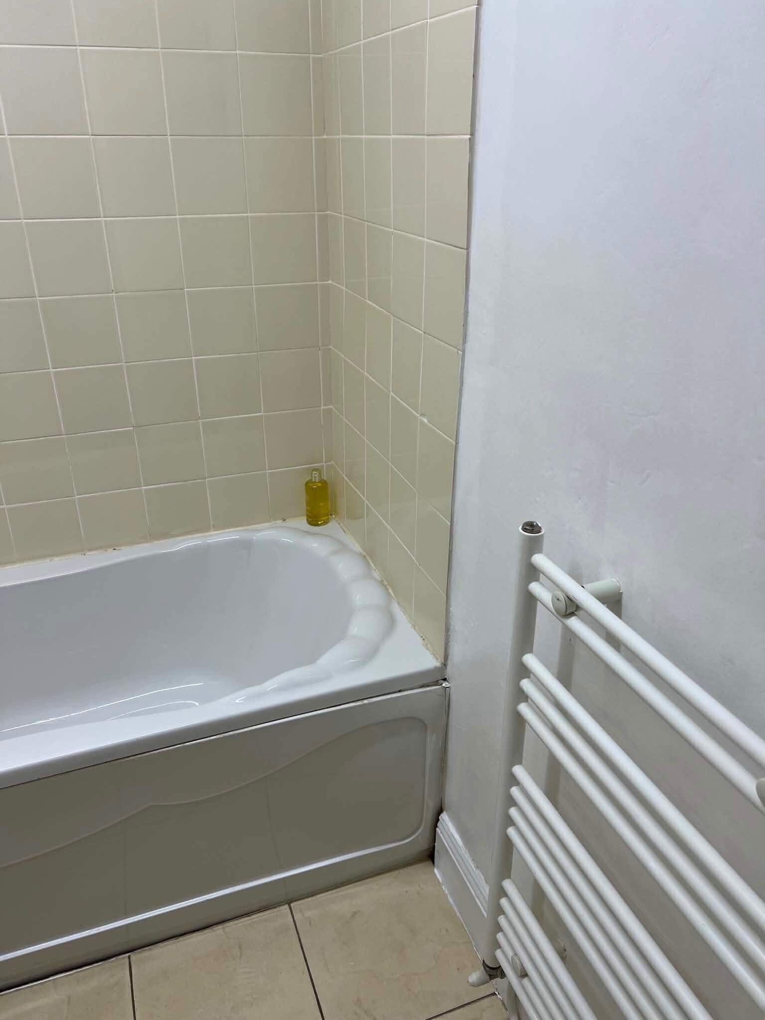 Een badkamer met een witte badkuip, een witte radiator en beige tegels.