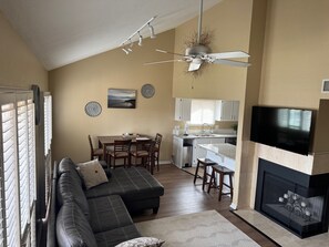 A living room with a sectional sofa, dining table, and chairs, a kitchen with a TV and fireplace, and a ceiling fan. - Spacious St. George Condo with Loft, Sleeps 10 (St. George)