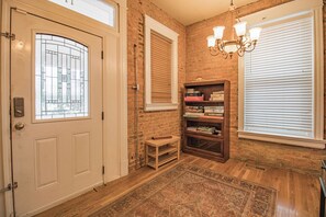 A room with a wooden floor, a white door with a glass panel, a brick wall, a bookshelf, and a chandelier. - 3 Story Home with Penthouse Suite (Kansas City)