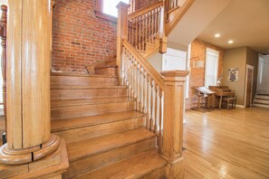 A wooden staircase with a brick wall background, a dining area with a table and chairs, and a door in the background. - 3 Story Home with Penthouse Suite (Kansas City)