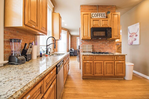 A kitchen with wooden cabinets, a granite countertop, a coffee sign, and a microwave. - 3 Story Home with Penthouse Suite (Kansas City)